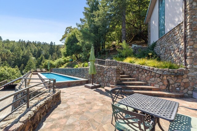 view of pool with a fenced in pool, outdoor dining area, a patio, and a wooded view