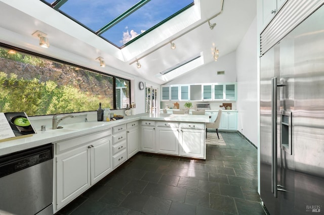 kitchen with stainless steel appliances, light countertops, white cabinets, a sink, and vaulted ceiling with skylight