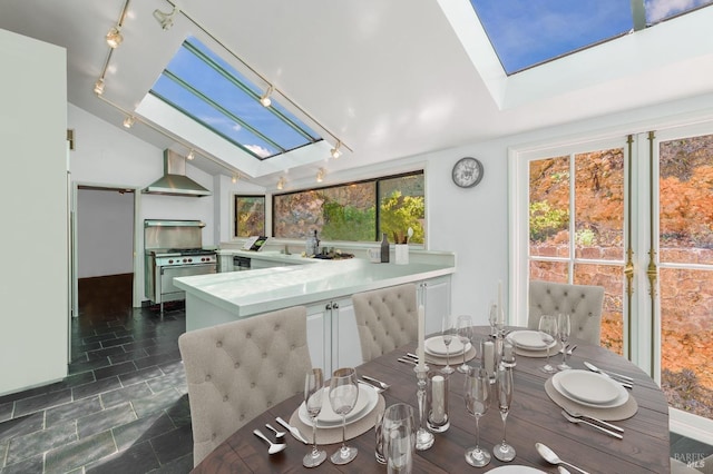 kitchen featuring a peninsula, wall chimney range hood, lofted ceiling with skylight, range with gas cooktop, and track lighting