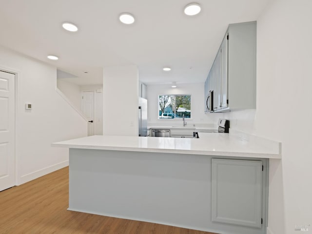 kitchen featuring stainless steel appliances, a peninsula, a sink, light countertops, and light wood-type flooring