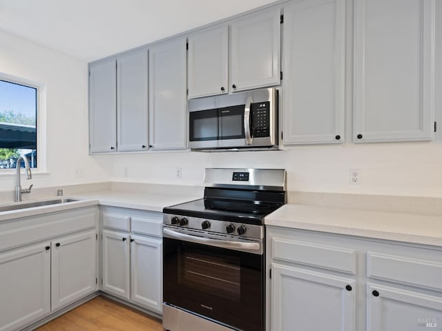 kitchen with appliances with stainless steel finishes, light countertops, a sink, and light wood finished floors