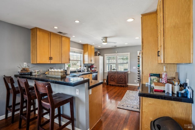 kitchen with visible vents, stainless steel dishwasher, dark wood finished floors, a peninsula, and a breakfast bar area