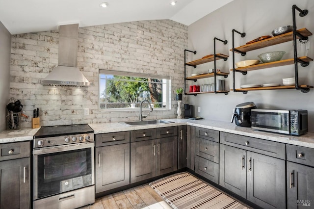 kitchen with a sink, open shelves, stainless steel appliances, wall chimney exhaust hood, and vaulted ceiling