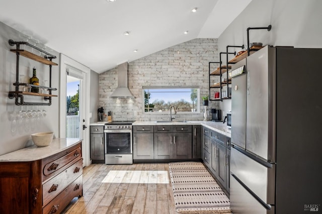 kitchen featuring open shelves, lofted ceiling, a sink, stainless steel appliances, and wall chimney exhaust hood