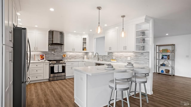 kitchen featuring stainless steel appliances, white cabinets, wall chimney range hood, a peninsula, and a kitchen bar