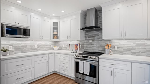 kitchen featuring white cabinets, decorative backsplash, wall chimney exhaust hood, light wood-style flooring, and stainless steel appliances