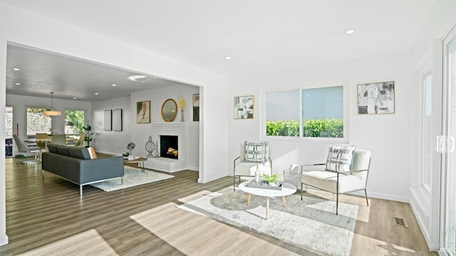 living room featuring recessed lighting, a brick fireplace, wood finished floors, and a healthy amount of sunlight