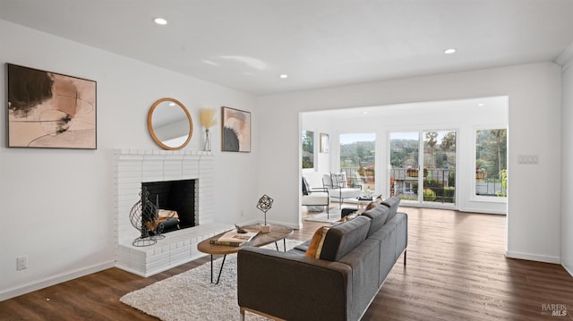 living room featuring a brick fireplace, baseboards, and wood finished floors