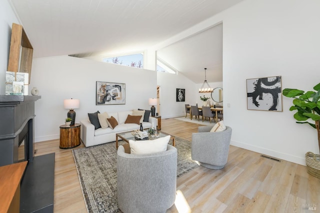 living area with visible vents, light wood-style flooring, an inviting chandelier, a fireplace with flush hearth, and baseboards