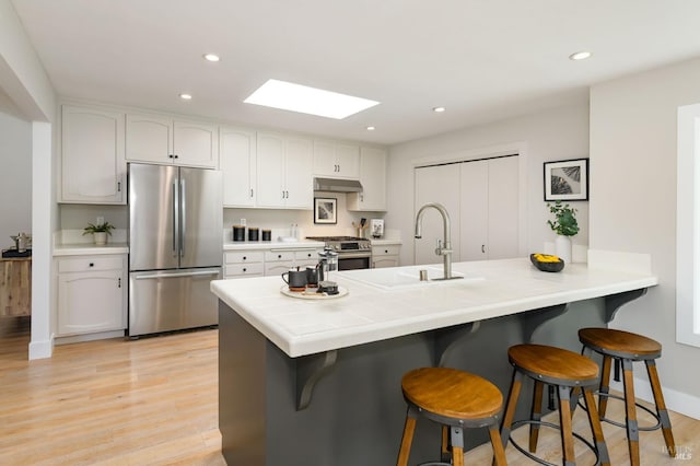 kitchen with a skylight, tile countertops, light wood-style flooring, stainless steel appliances, and a kitchen bar