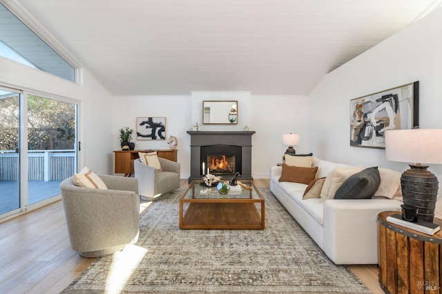 living room featuring lofted ceiling, a warm lit fireplace, and wood finished floors