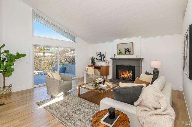 living room featuring lofted ceiling, visible vents, a glass covered fireplace, wood finished floors, and baseboards