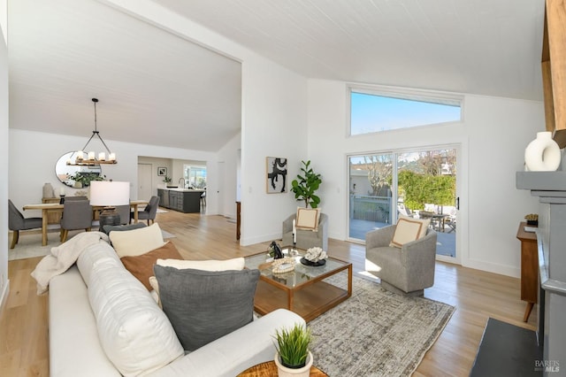 living area with vaulted ceiling, light wood-type flooring, a chandelier, and baseboards