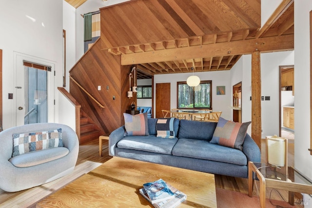 living room featuring a towering ceiling, wooden ceiling, stairway, wood finished floors, and beam ceiling