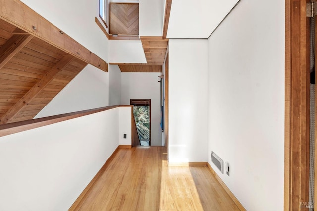 hall with baseboards, visible vents, wood ceiling, light wood-style flooring, and beam ceiling