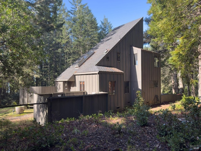 view of side of property featuring a shingled roof, board and batten siding, and fence