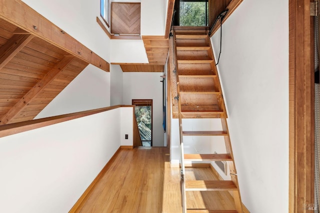 stairs featuring high vaulted ceiling, wooden ceiling, beamed ceiling, and wood finished floors