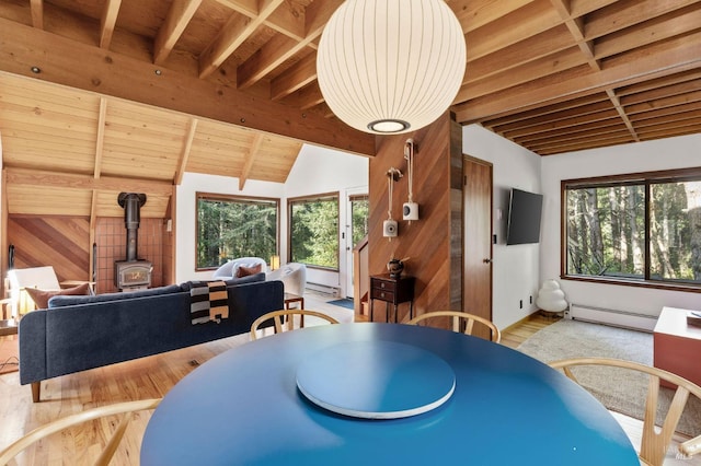 dining area with a baseboard heating unit, a healthy amount of sunlight, a wood stove, and vaulted ceiling with beams