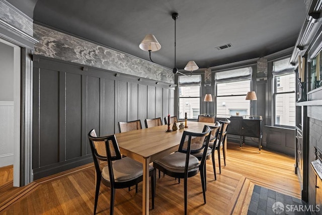 dining space featuring visible vents, wainscoting, light wood-style flooring, a fireplace, and a decorative wall