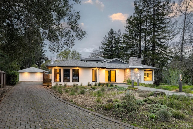 prairie-style home with a garage, stone siding, a chimney, an outbuilding, and fence