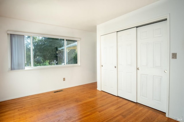 unfurnished bedroom featuring baseboards, a closet, visible vents, and wood finished floors