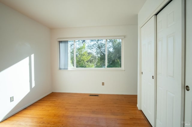 unfurnished bedroom featuring light wood-style floors, baseboards, visible vents, and a closet