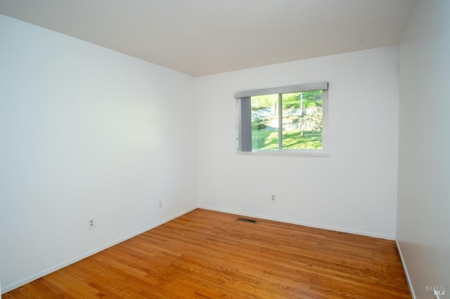 unfurnished room with light wood-style floors, visible vents, and baseboards