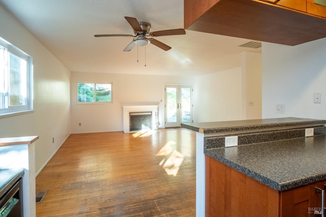 kitchen featuring dark countertops, light wood-style flooring, brown cabinets, french doors, and a brick fireplace