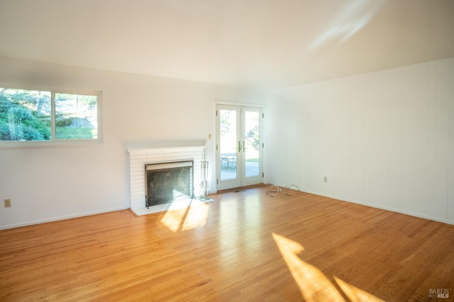 unfurnished living room with light wood-style floors, a fireplace, baseboards, and french doors