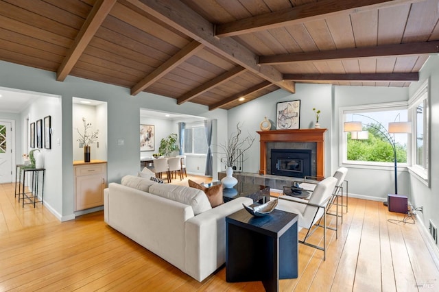 living area featuring lofted ceiling with beams, light wood-type flooring, wooden ceiling, baseboards, and a tile fireplace