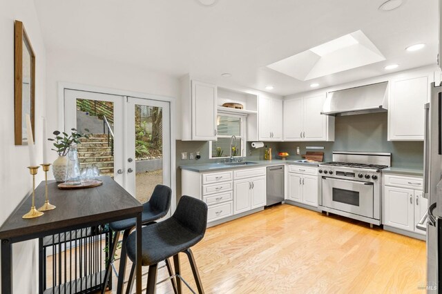 kitchen featuring a skylight, a sink, french doors, high end range, and wall chimney exhaust hood