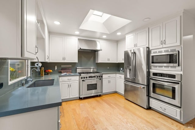 kitchen with a skylight, a sink, white cabinets, wall chimney range hood, and high end appliances