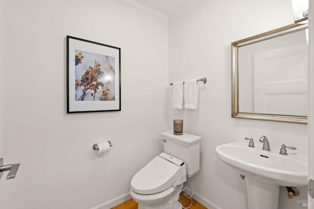 half bathroom featuring ornamental molding, a sink, toilet, and baseboards