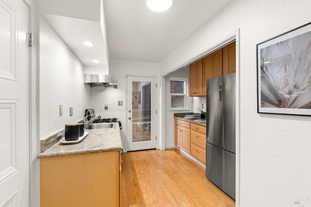 kitchen featuring brown cabinetry, light wood-style flooring, freestanding refrigerator, a sink, and recessed lighting