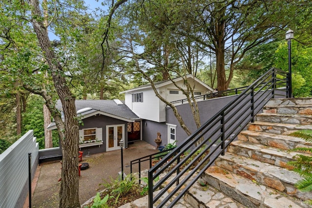 view of front of house with french doors, roof with shingles, stairway, a patio area, and fence