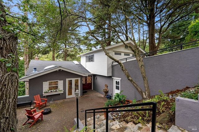 view of front of house featuring french doors, stucco siding, a shingled roof, a patio area, and a fire pit