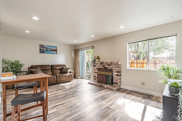 living area featuring visible vents, light wood-style flooring, a brick fireplace, a textured ceiling, and baseboards