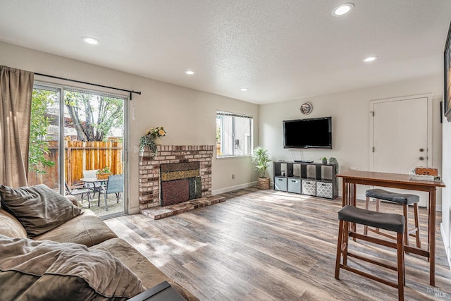 living room featuring recessed lighting, a brick fireplace, a textured ceiling, and wood finished floors