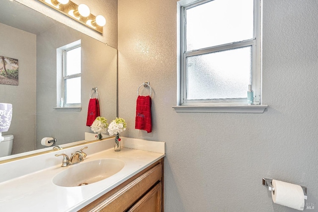 bathroom with toilet, a textured wall, and vanity