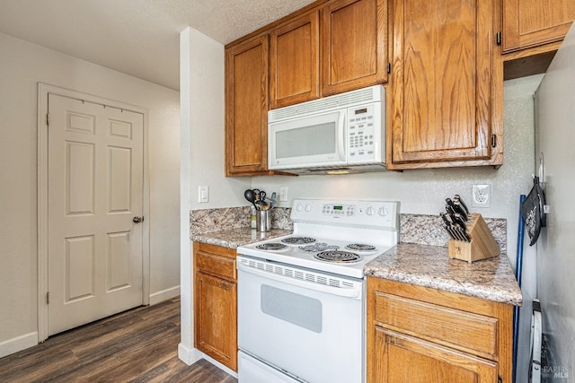 kitchen featuring dark wood-style floors, brown cabinetry, light stone countertops, white appliances, and baseboards