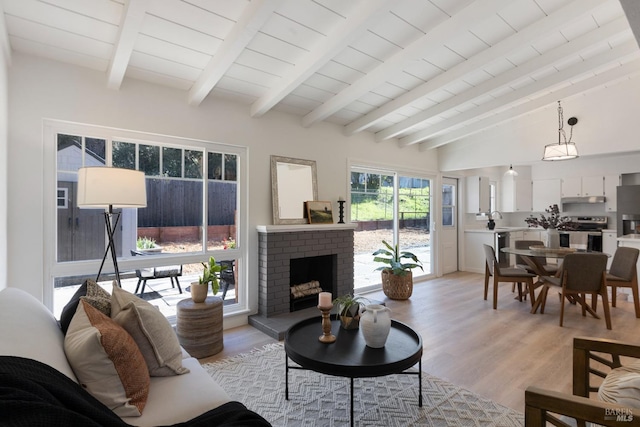 living area with lofted ceiling with beams, a fireplace, and light wood-style flooring