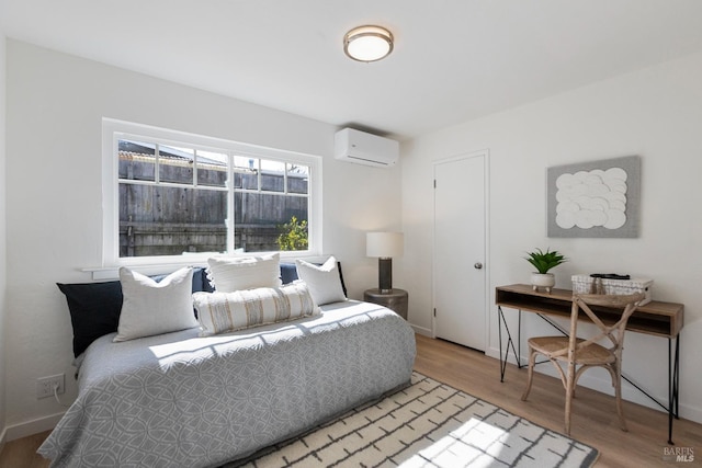 bedroom with a wall unit AC, wood finished floors, and baseboards