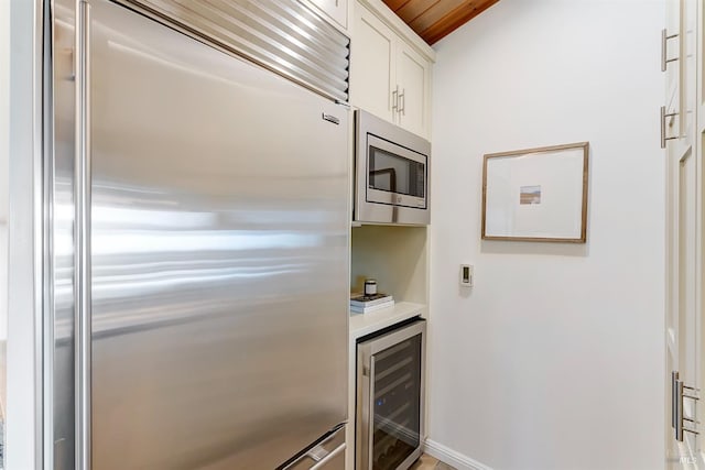 kitchen featuring built in appliances, beverage cooler, white cabinetry, baseboards, and light countertops