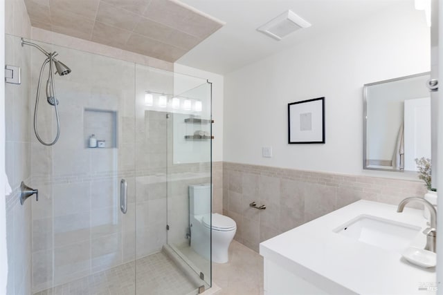 full bath featuring a stall shower, visible vents, toilet, vanity, and tile walls