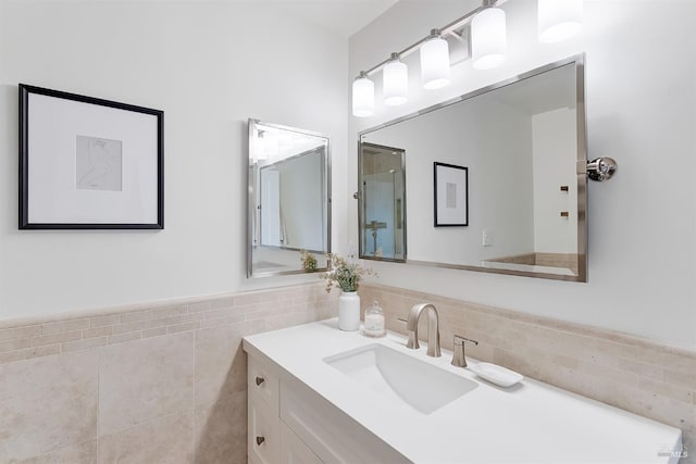 bathroom featuring wainscoting, a shower with shower door, tile walls, and vanity