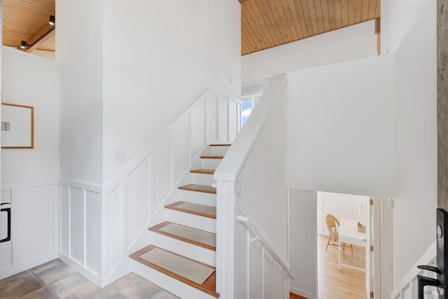 stairs with a wainscoted wall, wood ceiling, and a decorative wall