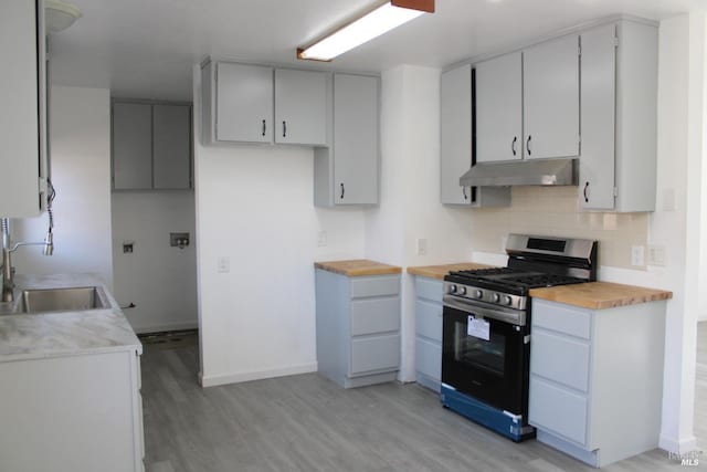 kitchen with under cabinet range hood, a sink, backsplash, light wood finished floors, and stainless steel range with gas stovetop