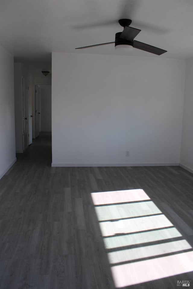 spare room featuring dark wood-type flooring, baseboards, and a ceiling fan