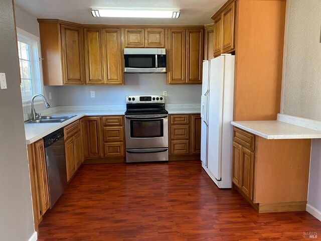 kitchen with stainless steel appliances, dark wood-type flooring, a sink, light countertops, and brown cabinetry