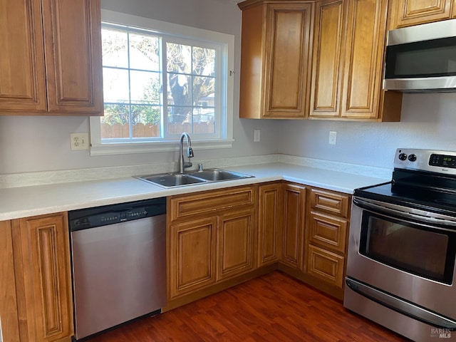 kitchen featuring brown cabinets, dark wood finished floors, light countertops, appliances with stainless steel finishes, and a sink